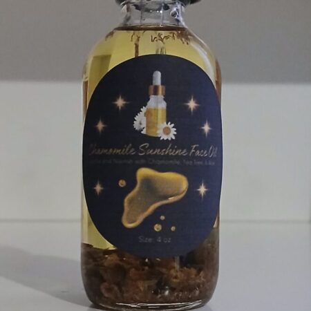 Chamomile Sunshine Face Oil in a glass bottle with chamomile flowers, aloe vera, and tea tree leaves on a wooden surface.